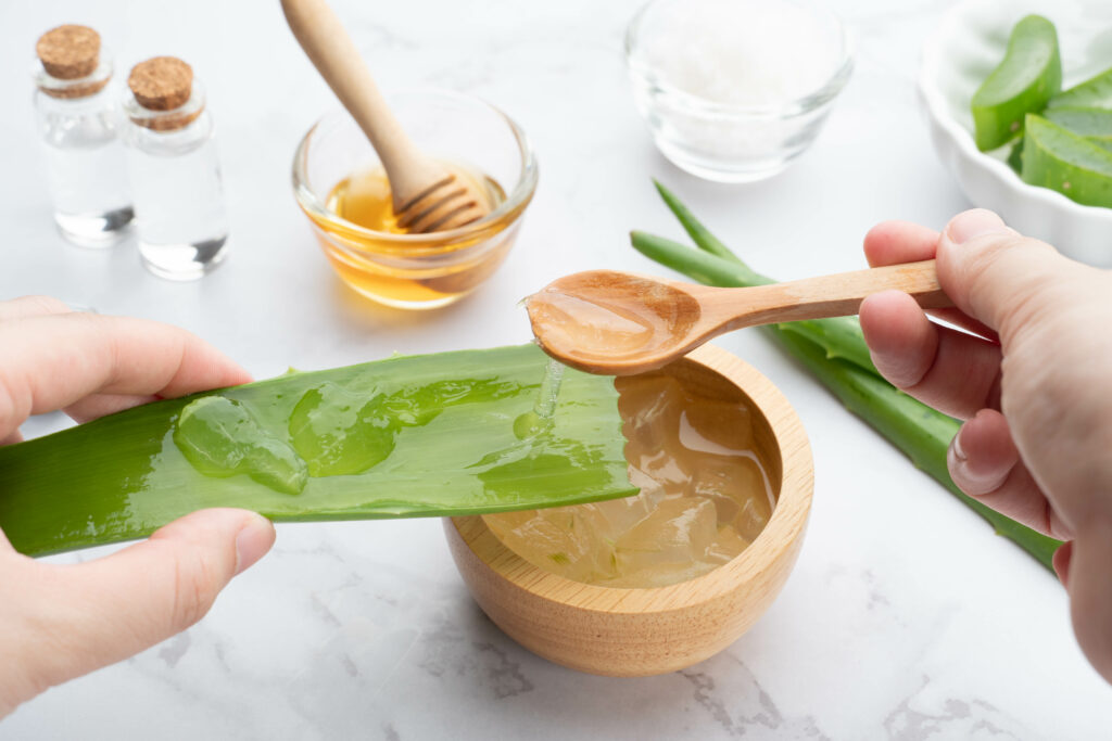 Natural homemade aloe vera gel face and body scrub for skin problems. DIY Recipe for sunburn, acne and dry skin. Hands of woman preparing aloe vera gel with honey, sea salt and essential oil.