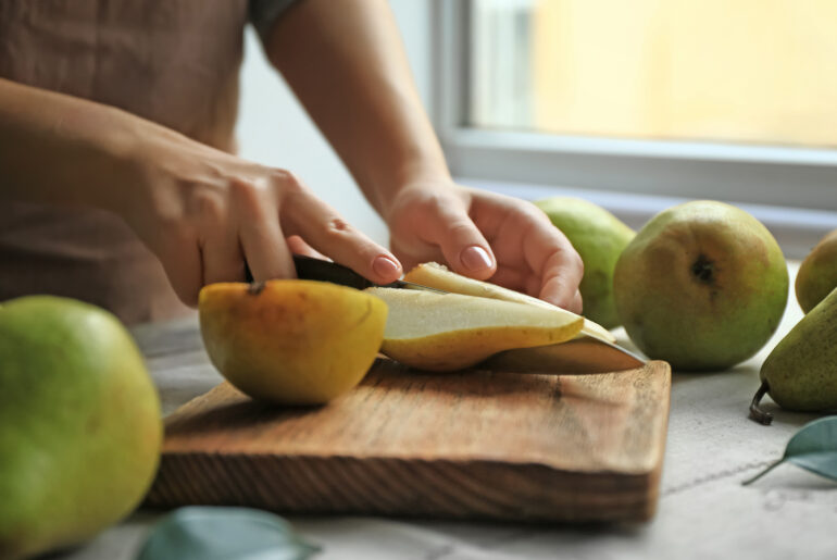 Woman cutting ripe pears on table