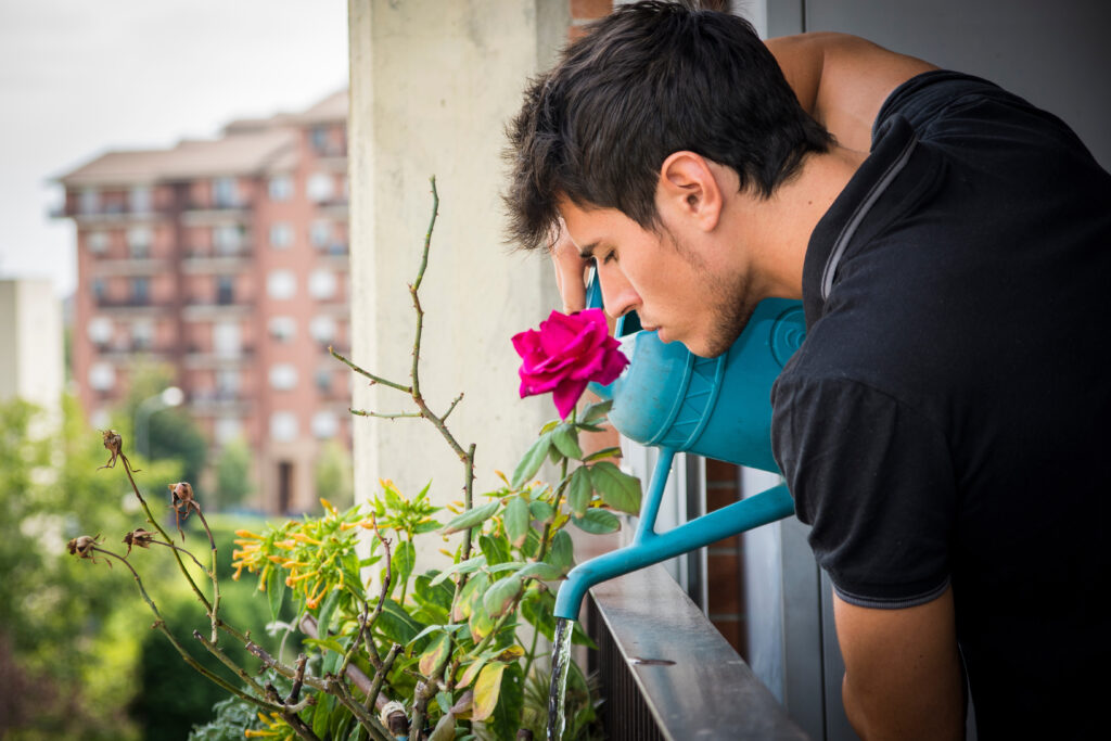 Young Man Watering Plants on Apartment Balcony