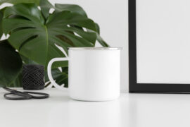 Enamel mug mockup with workspace accessories and a monstera plant.