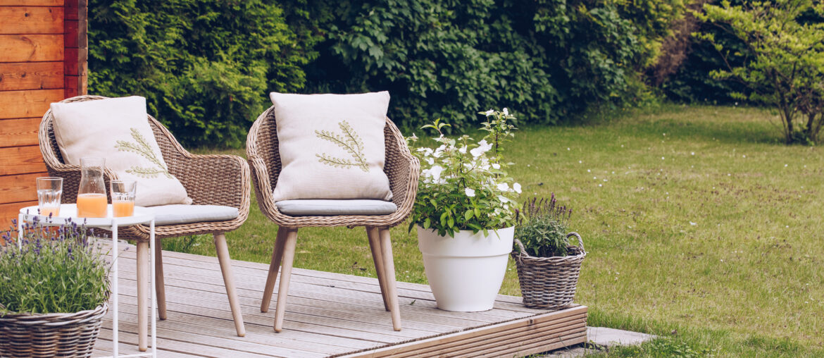 2 woven garden chairs outside in the garden with lots of trees and flowers. Rest in the garden. Cottage with garden. Vacation at home