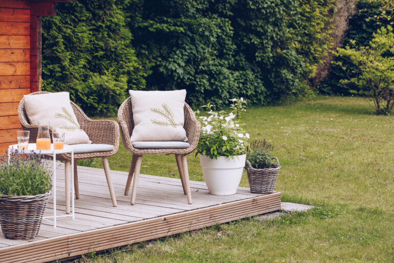 2 woven garden chairs outside in the garden with lots of trees and flowers. Rest in the garden. Cottage with garden. Vacation at home